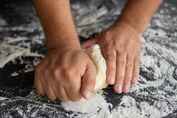 chef cooks pizza dough, strong male hands knead raw ingredients