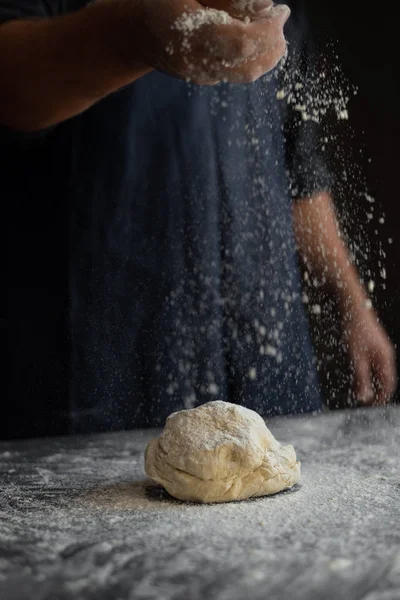 Αρσενικό σεφ ψεκάζει αλεύρι σε ακατέργαστη ζύμη με τα χέρια του. — Φωτογραφία Αρχείου