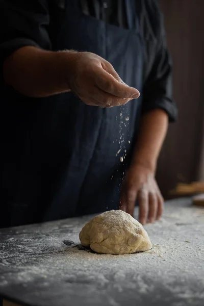 chef cooks cake for pizza, male hands sprinkle raw dough with flour