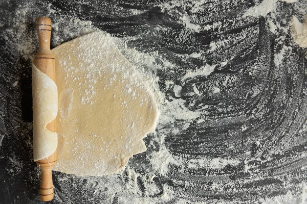 En stor kaka av rå deg, en brödkavel gjord av trä ligger på ett bord, strö vetemjöl — Stockfoto