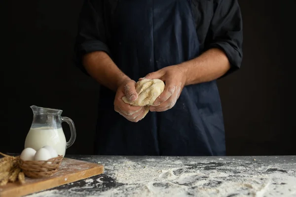 Чоловічі кухарські руки замішують тісто в робочому фартусі на чорному тлі — стокове фото