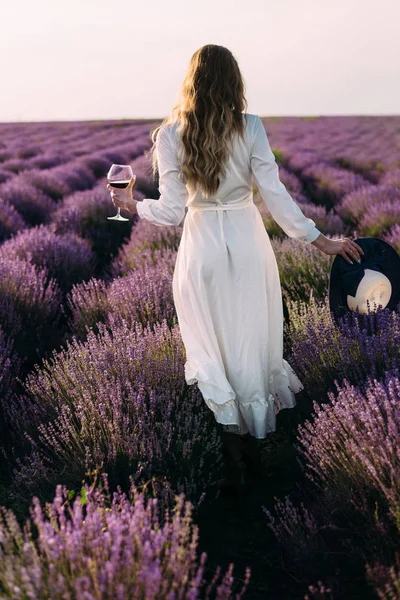 野餐在大自然中，一个年轻的美丽的女孩站在薰衣草的田野上，一杯葡萄酒，女性的手 — 图库照片