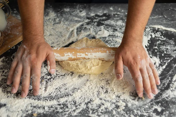 the chef rolls the dough with a rolling pin, an ingredient for making pizza.