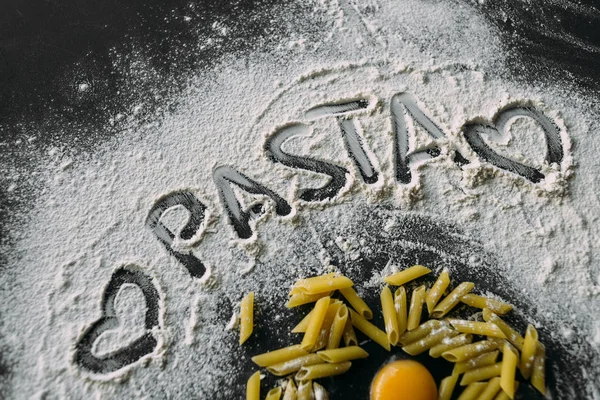 A pasta de inscrição na farinha e dois corações próximos, um ovo de frango cru , — Fotografia de Stock