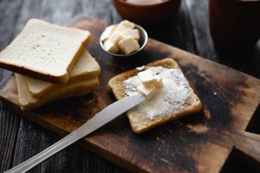 Mutfak masası, masada bir parça ekmek, kabuklu ve tereyağlı bir tost, bir bıçak ve bir kesim tahtası.