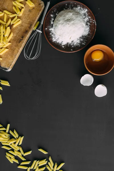 On a black background food, raw pasta, eggs and flour. — Stock Photo, Image