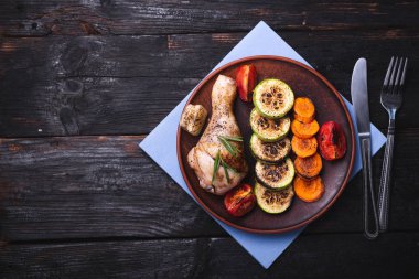Lezzetli ızgara tavuk budu, tabakta fırında sebze. Tahta masa.,