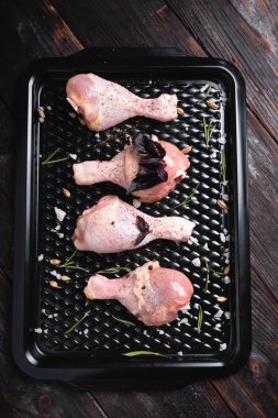 Siyah bir arka plan üzerinde tavuk bacakları. Tabakta taze çiğ tavuk bacağı aranjmanı. Üstte görüntü.