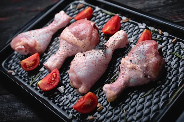 我们煮烤鸡腿，腌肉在黑暗的烤盘，香香料和西红柿 — 图库照片