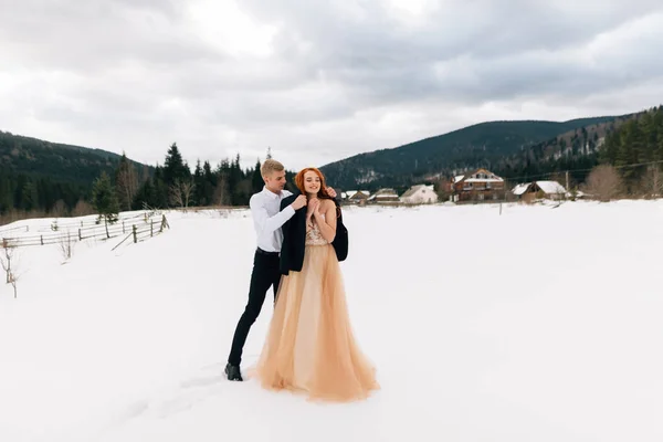 Boda en invierno, el novio calienta a su amada novia. Usando una chaqueta para una niña, nieve y paisajes de invierno — Foto de Stock