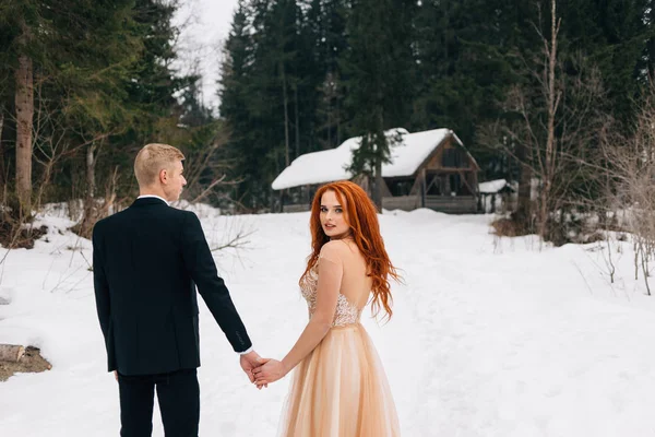 Mooie roodharige meisje in de winter jurk houden van een jongens hand. Bruid en bruidegom, bruiloft in de winter. — Stockfoto