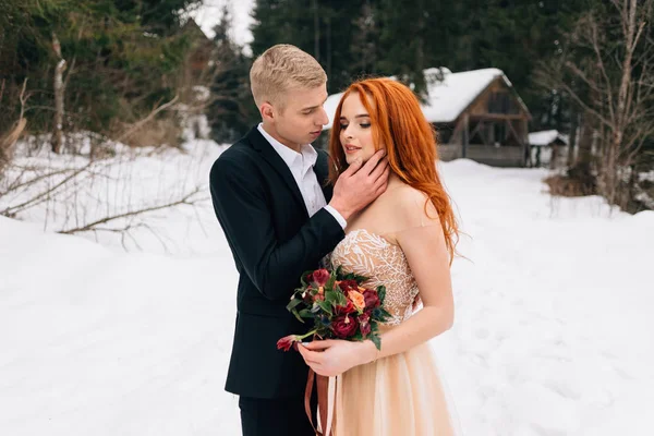 冬の結婚式では、新郎新婦は雪の上に森の中に立っています。彼は彼女のほおをそっと打つ. — ストック写真