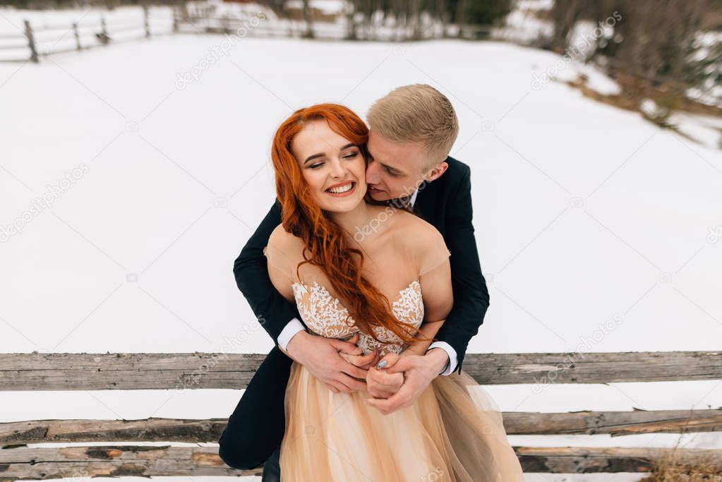 Sensitive portrait of cheerful beautiful newlyweds. The groom warms hugs his bride with red hair.