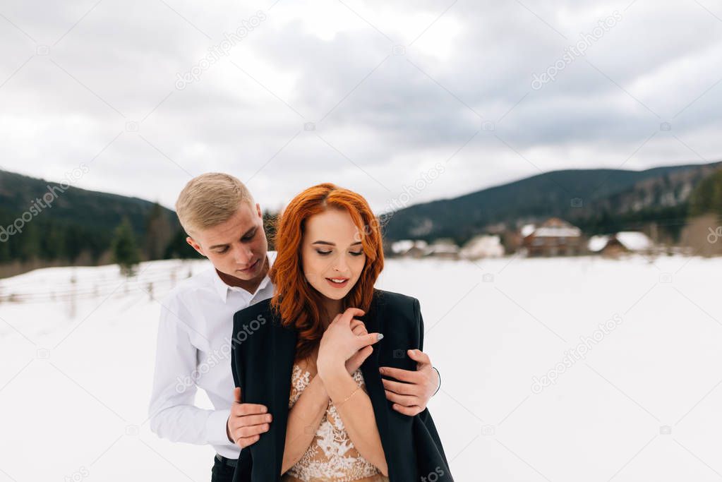 wedding in winter, a young stylish man hugs a beautiful and tender bride. Girl with red hair.