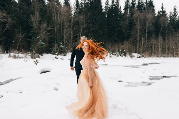 Mooie mannen en vrouwen in trouwjurken, bruiloft in de winter. Stijlvolle bruid en bruidegom rennen en genieten van het leven in de sneeuw. — Stockfoto