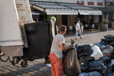 Şehir sokaklarındaki çöpleri temizleyen bir adam çöp poşetlerini bir çöp kamyonuna yüklüyor..