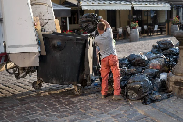 Městský dělník na ulicích města sbírá odpadky ve velkých černých pytlích a nakládá je do popelářského vozu — Stock fotografie