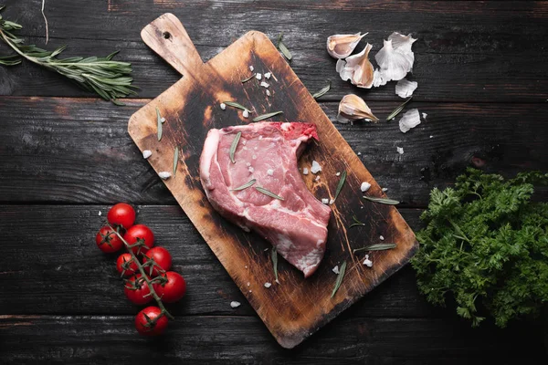 A raw piece of meat lies on the table, fragrant spices, tomatoes and herbs. — Stockfoto