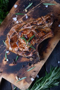 Kesme tahtasında büyük bir parça kızarmış et, baharatlar ve aromatik otlar..