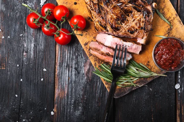 Хорошо зажаренный говяжий стейк на деревянной доске, свежие овощи на столе — стоковое фото