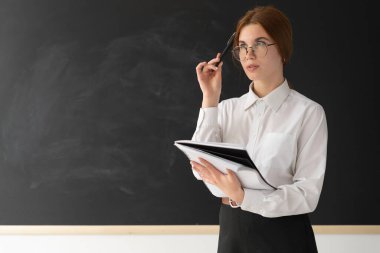 Gözlüklü genç ve güzel bir öğretmen bir tahtanın önünde duruyor. Onun elinde bir defter var. Düşünüyor. Eli yüzüne yakındır. Tahta yazıtlardan temizlenmiş. Kız üzerine bir şeyler yazacak. Yazacak bir yer..