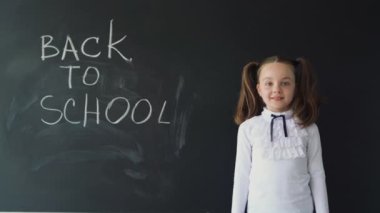 Üniformalı genç bir kız tahtanın önünde duruyor. Okula geri dönmek için karatahta yazısı. Eğitim ve eğitim süreci.