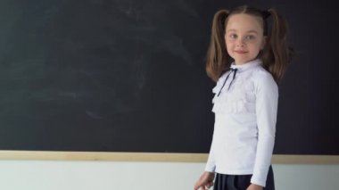 Tahtanın yanında genç bir üniversite öğrencisi. Genç bir kızın üzerinde okul üniforması. Tahta temiz ve siyah. Yazı için uygun bir yer. Eğitim kavramı.