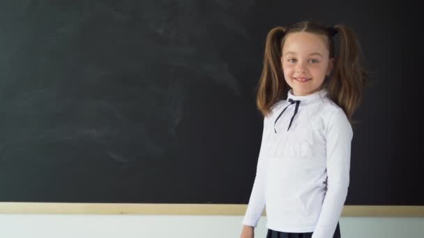 Hermoso estudiante universitario inteligente cerca de la pizarra. En un uniforme de chica joven. El tablero es limpio y negro. Lugar para una inscripción. El concepto de educación . — Vídeos de Stock