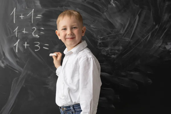 男子生徒は教室の黒板に立ち 数学の例を書く その少年は笑っている 授業では積極的な学生 学校に戻る 小学校での数学の授業 黒板に口頭で答えなさい テキストの場所 — ストック写真