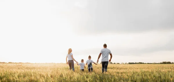 Mutlu aile: anne, baba, çocuklar, gün batımında doğada iki oğul. Sahada dolaşıyorlar. Açık hava eğlencesi. Gözlerde mutluluk var. Mısır gevreği topla. Metin için yer