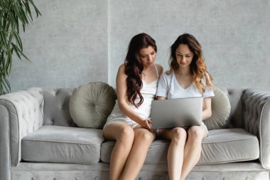 İki genç kız kardeş kanepede bir odada oturuyor ve bir dizüstü bilgisayardan İnternet 'ten alışveriş yapıyorlar. Esmerler, bol saçlı ve beyaz pijama giyiyorlar. Evden çıkmadan kızlar için alışveriş yapmak. Kız kardeşimle evde bir gün..