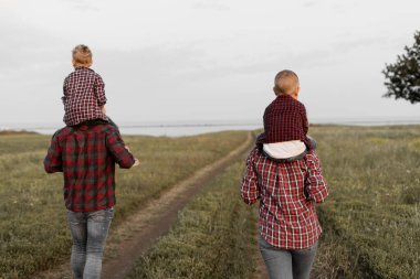 Dikiz aynasından mutlu bir aile doğada yürüyor. Anne, baba, iki çocuk. Temiz havada yürü. Ebeveynler çocuklarını omuzlarında taşırlar..