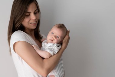 Güzel, genç bir anne kucağında küçük bir çocuk tutuyor. Bir oğlana iki ay. Metin için beyaz duvar alanı.