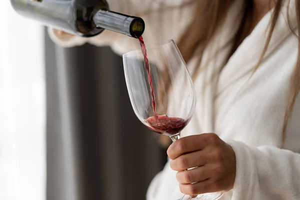 女性の手にボトルを閉じます 赤ワインをグラスに注ぐ ホテルの部屋で女性 バスローブ — ストック写真