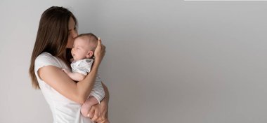 Güzel, genç bir anne kucağında küçük bir bebek tutuyor. Beyaz duvar kopyalama alanı. Metin için yer