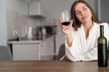 Genç ve güzel bir kadın mutfakta oturuyor. Akşam işten sonra şarap içmek için. İçkinin tadına bakıyorum..