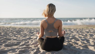Genç ve güzel bir kadın okyanusta oturuyor. Sabah meditasyonu. Doğayla olan sakinlik ve birlik.