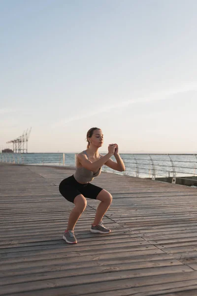 Dívka se angažuje ve fitness na mořském břehu či oceánu, přikrčí se, v ranním světle koncept aktivního životního stylu. — Stock fotografie