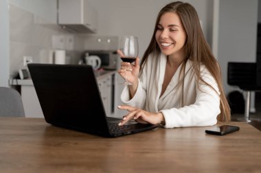 Online parti konsepti. Kafkas görünümlü genç bir kadın web kamerasıyla iletişim kuruyor. Elinde bir kadeh kırmızı şarap tutuyordu. Dinlen. Ev eşyaları..