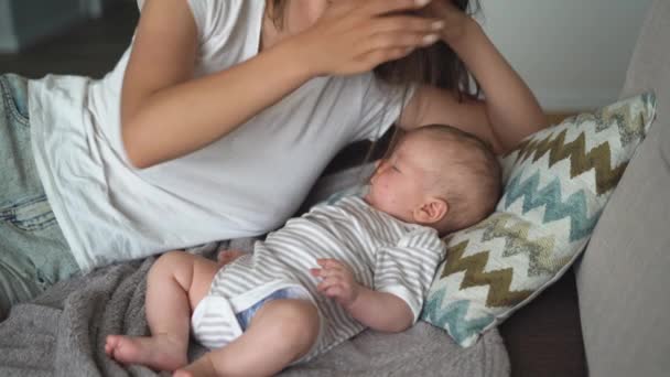 Egy gyönyörű fiatal anya fekszik egy szoptató baba mellett, egy nő és egy fiú nevetnek.. — Stock videók
