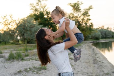 Kollarında bir kızı olan bir anne. Başının üstünde, anne kızını kaldırdı. Kız, annesinin yüzüne tutunuyor. Birbirlerinin gözlerinin içine bakarlar. Onların her ikisi de mutlu. Onlar bir göletin kıyısındalar. Bir sürü yeşillik var..
