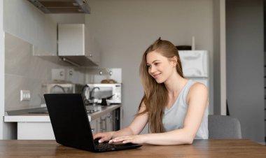 Mutfakta dizüstü bilgisayarını kullanan güzel bir kadın. Karantina bölgesinde evden çalışıyor ya da ders çalışıyor. Sosyal uzaklık, teknoloji kavramı