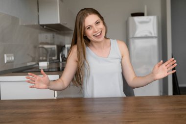 Pozitif, güzel bir kadın, mutfağındaki web kamerasından sohbet ederken ellerini kaldırıyor. Çevrimiçi iletişim kavramı