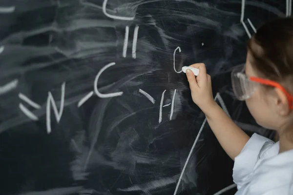 女の子の手のクローズアップ 白いチョークを持ち 化学のレッスンで式を書きなさい 賢い子の概念 — ストック写真