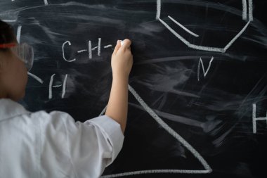 Bir kızın eline yakın çekim. Beyaz tebeşiri tut ve kimya dersinde formüller yaz. Tahta. Okul konseptine geri dönelim. Çevrimdışı eğitim