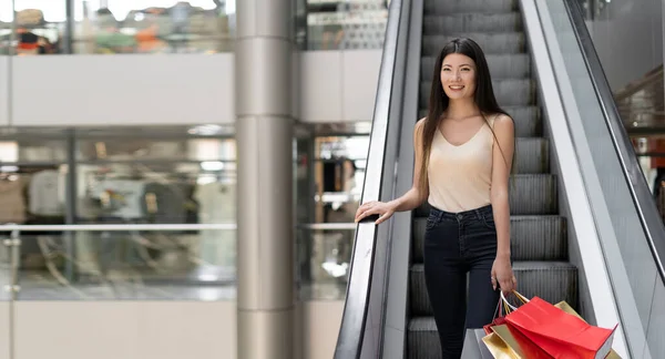年轻美丽的韩国女人走下林荫道的扶梯 明亮的购物袋 文字的位置 复制空间 — 图库照片