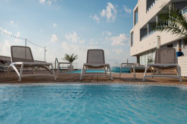 Havuzun kenarında üç boş güneş pansiyonu duruyor. Sıcak ülkelerde dinlenmek. Metin için yer.