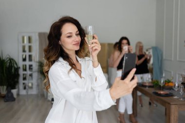 Genç bir kadın parti sırasında bir bardak şampanyayla selfie çeker. şirket, tatiller ve tatil konsepti - mutlu arkadaşlar veya parti aksesuarları ile takım