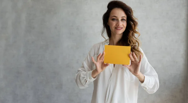 woman holding paper in her hands. Model of the Caucasian race, isolated on a gray background with a leaf in her hands. Horizontal image. Naturally, no makeup.