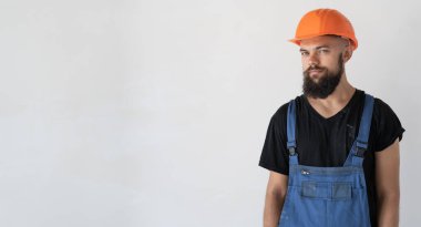 Erkek müteahhit özel kıyafetler giyer ve turuncu bir şapka beyaz bir duvarın yanında durur. Boşluğu kopyala